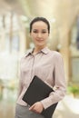 Smiling confident young woman holding a file indoors, looking into camera Royalty Free Stock Photo