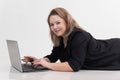 Smiling and contemplating blond woman lying on floor, using laptop for job, white background. Working on her new article Royalty Free Stock Photo
