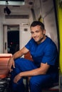 Smiling corpsman in uniform sits and squints in the ambulance car beside stretcher