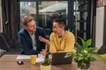 Smiling couple of diverse businesspeople doing paperwork discussing and working on laptop computer while sitting at a table in