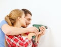 Smiling couple drilling hole in wall at home