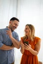 Smiling couple embracing while using a smartphone. People sharing social media on mobile phone.