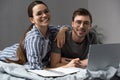 Smiling couple in glasses writing in notepad and working on laptop while lying