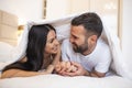 Smiling couple going to kiss under sleeping sheets in the morning. In love young happy couple lying in bed in the morning Royalty Free Stock Photo