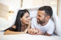 Smiling couple going to kiss under sleeping sheets in the morning. In love young happy couple lying in bed in the morning Royalty Free Stock Photo