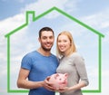 Smiling couple holding piggy bank over green house Royalty Free Stock Photo