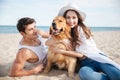 Smiling couple in love sitting on the beach with dog Royalty Free Stock Photo