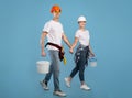 Smiling couple of painters holding hands walking with paint buckets, blue background