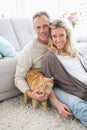 Smiling couple petting their gringer cat on rug Royalty Free Stock Photo