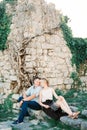 Smiling couple sitting on stone steps in the garden near the stone wall of an ancient castle Royalty Free Stock Photo