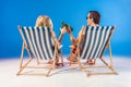 Smiling couple in sunglasses toasting with beer bottles resting in deck chairs