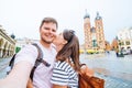 smiling couple taking selfie at krakow square market church saint mary on background