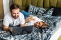 Smiling young couple using a laptop lying on their bed Royalty Free Stock Photo