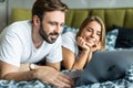 Smiling young couple using a laptop lying on their bed Royalty Free Stock Photo