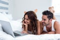 Smiling couple using laptop while lying under blanket Royalty Free Stock Photo