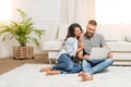 Smiling couple using laptop while sitting on carpet at home Royalty Free Stock Photo