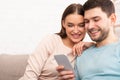 Smiling Couple Using Mobile Phone Sitting On Sofa Indoor Royalty Free Stock Photo