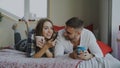Smiling couple watching TV while lying in bed and drinking coffee at home in the morning