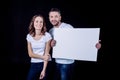 Smiling couple in white t-shirts holding blank white card and looking at camera Royalty Free Stock Photo