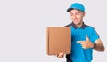 Smiling courier in blue uniform and a cap is pointing to the parcel he must deliver it to destination.