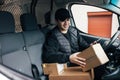 Smiling courier sitting on a driver`s seat checking delivery information on mobile phone while holding box