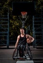 Smiling cripple basketball player in wheelchair holds a ball on open gaming ground.