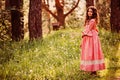 Smiling curly child girl in pink princess dress on the walk in summer forest