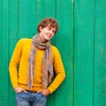 Smiling curly man in yellow sweater and scarf on green wooden ba