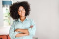 Smiling curly woman standing in modern apartment and looking aside dreamly