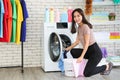 A smiling and cute Asian woman carrying a laundry basket and posing beside the washing machine Royalty Free Stock Photo