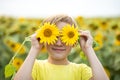 Smiling cute kid boy teen standing on a field and holding near by eyes sunflowers. Summer holiday. happy childhood Royalty Free Stock Photo
