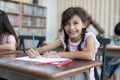 Smiling cute kid girl drawing with color pencil on white paper in art study class at elementary school Royalty Free Stock Photo