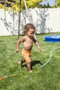 Smiling Cute little boy splashing through the sprinklers in the backyard