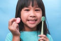 Smiling cute little girl holding toothbrush and sweets isolated on blue background. Kid training oral hygiene and Unhealth eat.