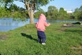 Smiling cute playful little girl is standing on green grass. girl toddler walks around the lake learns to walk. sunny Royalty Free Stock Photo