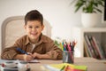 Smiling cute small european boy sitting at table, draws picture, look at camera in school, children garden room Royalty Free Stock Photo