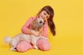 Smiling cute small girl wearing rosy attire sitting on floor against yellow wall, child looking at Pekingese dog and hugging it, Royalty Free Stock Photo