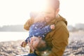 Smiling dad in the bright sunlight hugs a small child in a blue overalls with an apple in his hand to his chest. Close