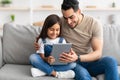 Smiling dad and daughter sitting on couch, using tablet Royalty Free Stock Photo