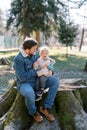 Smiling dad with a laughing little girl on his knees sits on a huge stump in a sunny meadow Royalty Free Stock Photo