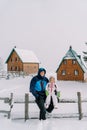 Smiling dad with a little girl on his lap sits on a fence in a village under snowfall Royalty Free Stock Photo