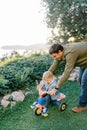 Smiling dad pushes a little girl riding a tricycle in the park