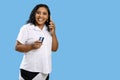 Smiling dark-skinned woman talks on cell phone holding a credit card, isolated on blue background