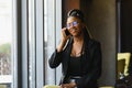 Smiling dark skinned woman in trendy wear laving cafe talking on mobile phone via roaming tariffs,african american millennial Royalty Free Stock Photo