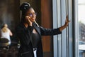 Smiling dark skinned woman in trendy wear laving cafe talking on mobile phone via roaming tariffs,african american millennial Royalty Free Stock Photo