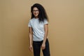 Smiling dark skinned young woman with glad face expression, wears optical glasses, white t shirt and jeans, poses carefree against Royalty Free Stock Photo