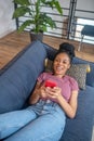 Smiling darkskinned woman with smartphone on sofa