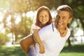 Smiling daughter piggyback riding her daddy in the park and looking at the camera