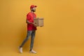 Smiling delivery man in red uniform and cap carrying a cardboard box Royalty Free Stock Photo