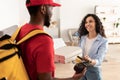 Smiling deliveryman holding POS machine, woman paying with bankcard